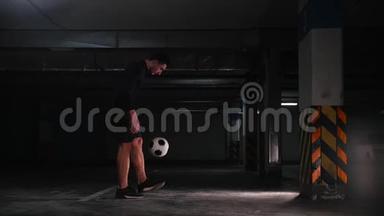 地下停车场。 运动足球男子训练他的足球技能。 把球从墙上踢下来